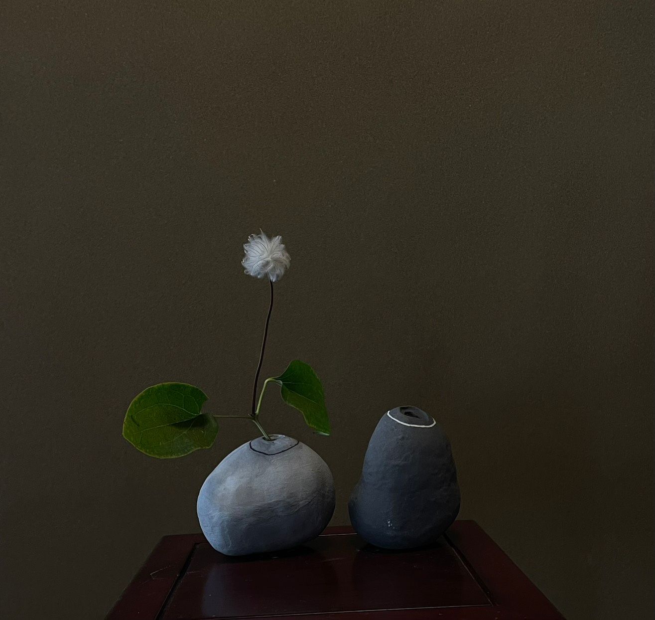 草花を一輪挿した、石ころのような青灰色の器ふたつ